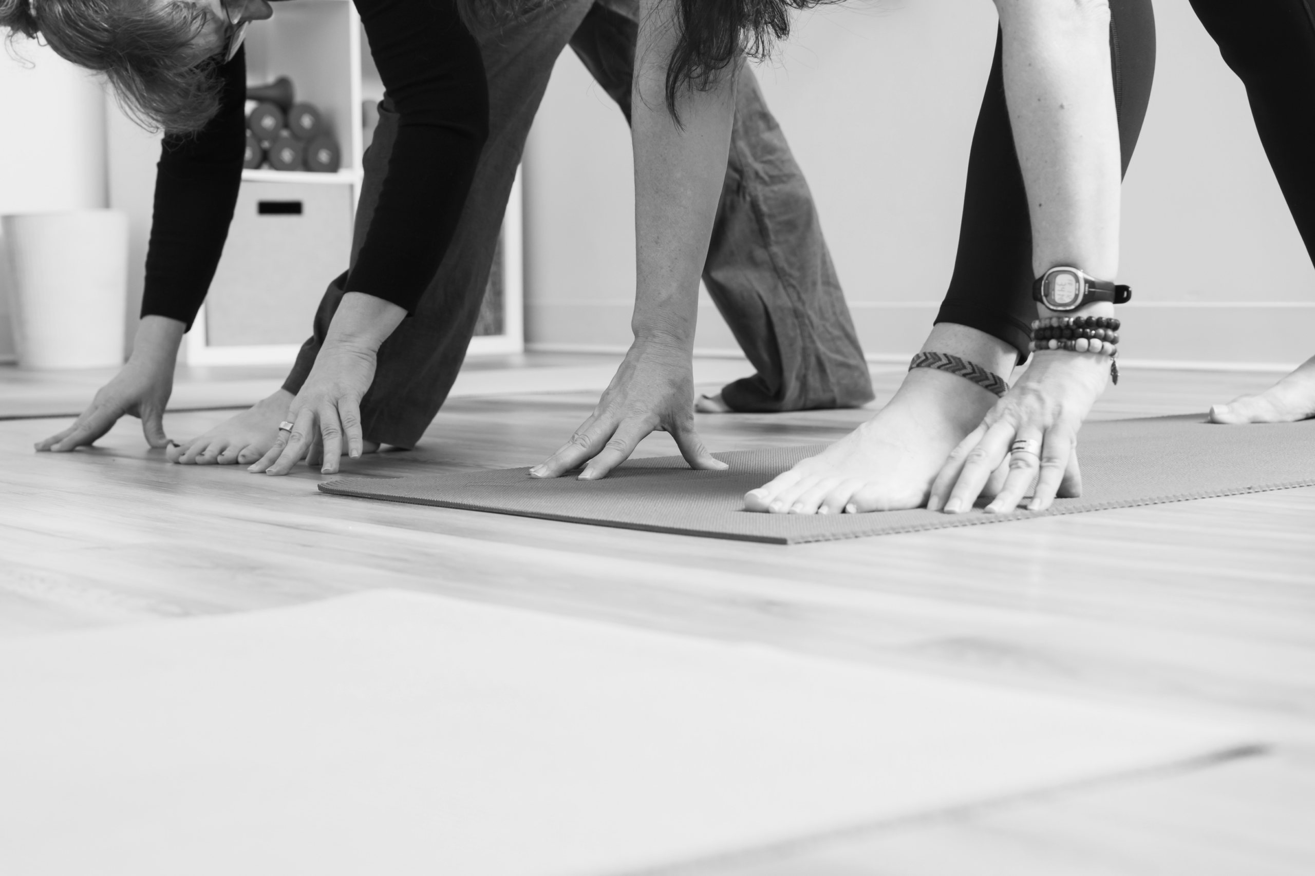 Close-up of hands reaching toward feet during a mat Pilates forward fold on studio mats.