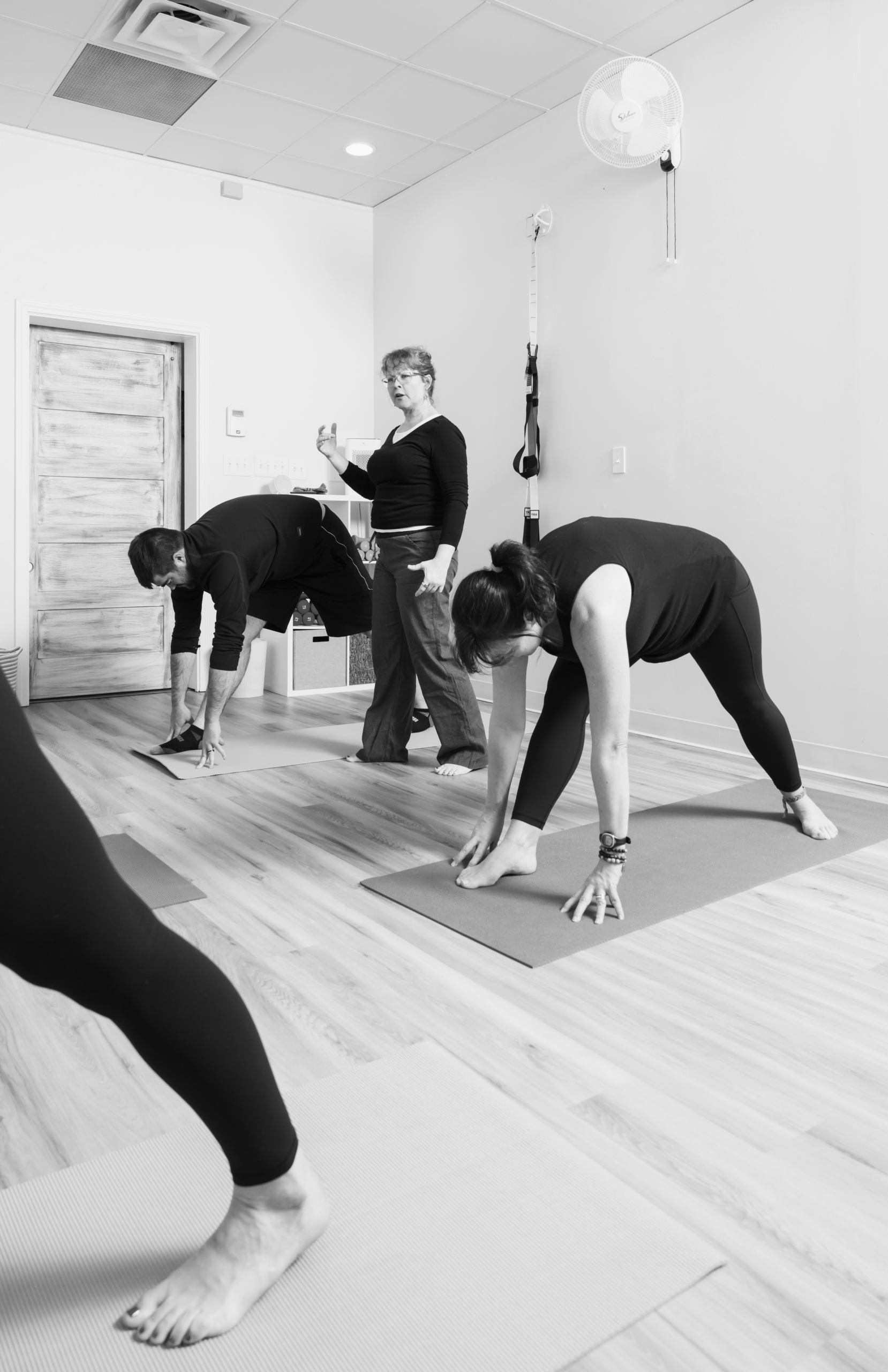 Pilates instructor guiding a small group through a forward-bend stretch on mats in a studio.